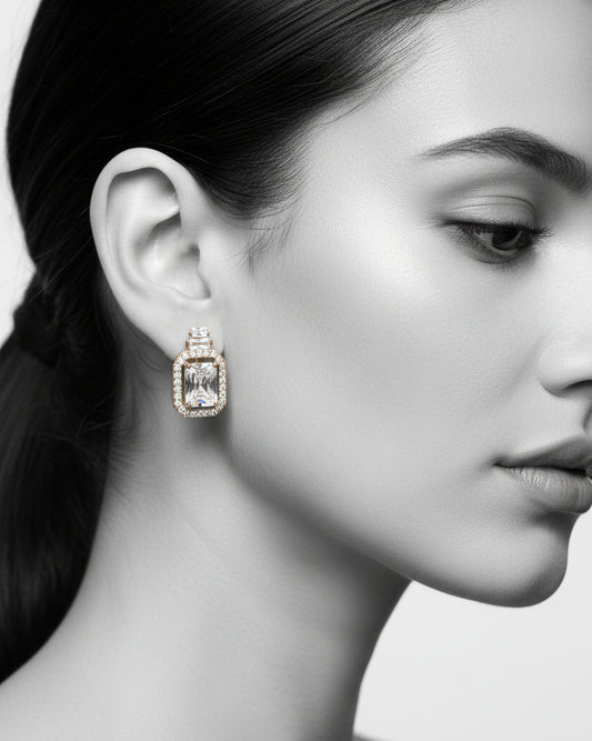 Diamond earrings held by a hand against a neutral background
