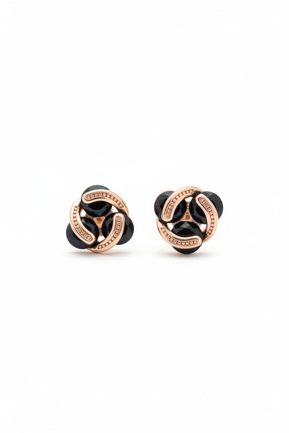 Pair of delicate rose gold interlocking stud earrings with glossy black stones held between fingers for size reference.
