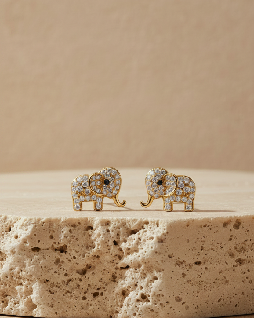 A pair of gold-plated elephant stud earrings fully encrusted with brilliant white cubic zirconia stones, displayed beautifully on a black fabric background.