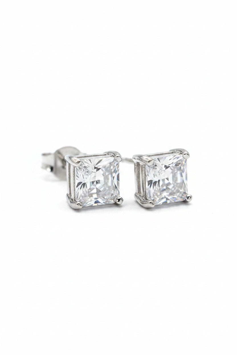 Pair of elegant princess cut square silver solitaire stud earrings displayed on a premium black fabric background.
