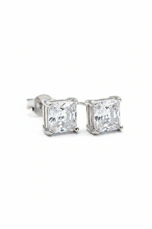 Pair of elegant princess cut square silver solitaire stud earrings displayed on a premium black fabric background.

