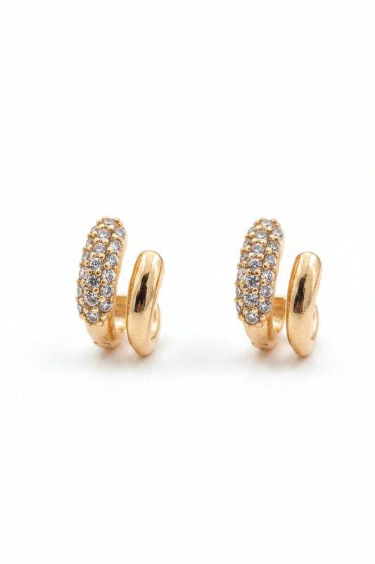 Top angle view of unique gold-plated C-cuff stud earrings featuring one row embedded with tiny white stones and a parallel smooth gold wave on black fabric.
